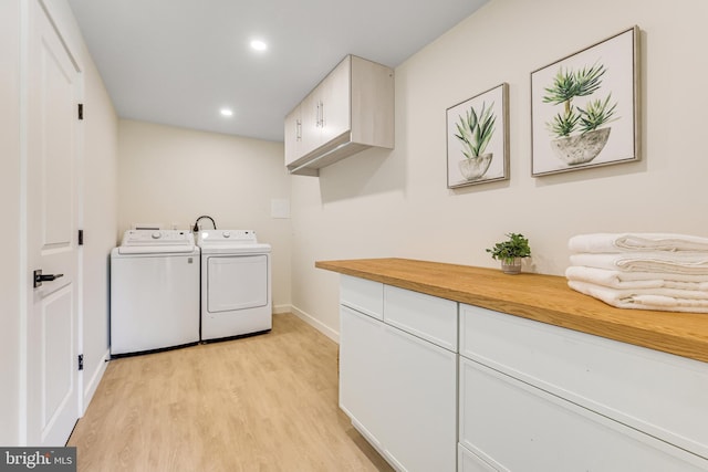 laundry room featuring washing machine and clothes dryer, cabinets, and light wood-type flooring