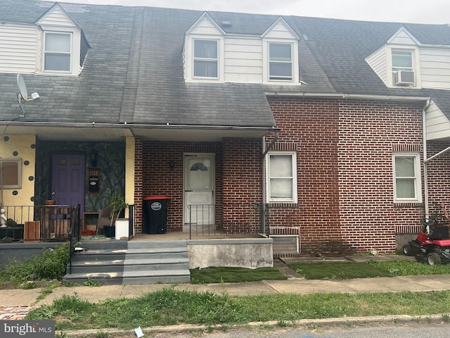 view of front facade with covered porch, brick siding, and cooling unit