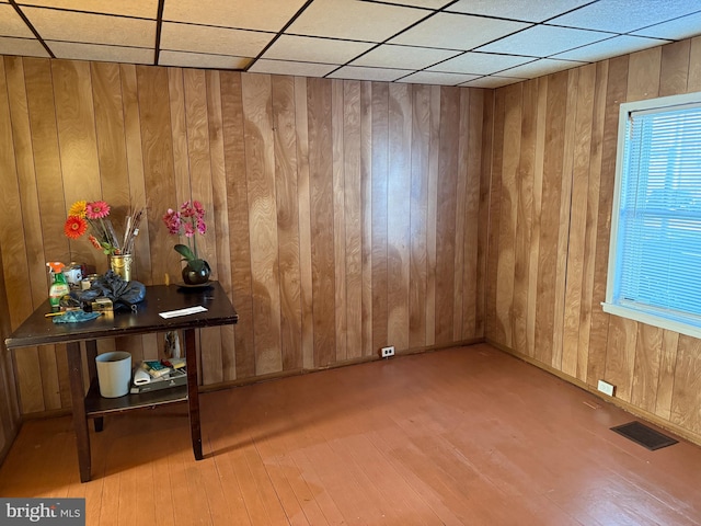 interior space with a paneled ceiling, visible vents, wooden walls, and wood finished floors