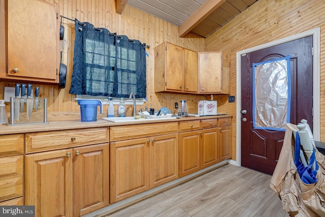 kitchen with light wood-type flooring, sink, beam ceiling, and wooden walls