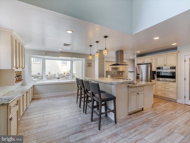 kitchen featuring hanging light fixtures, stainless steel appliances, island exhaust hood, a kitchen bar, and light hardwood / wood-style flooring