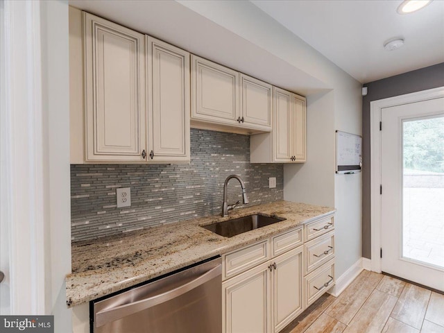 kitchen featuring backsplash, light stone countertops, cream cabinetry, stainless steel dishwasher, and a sink