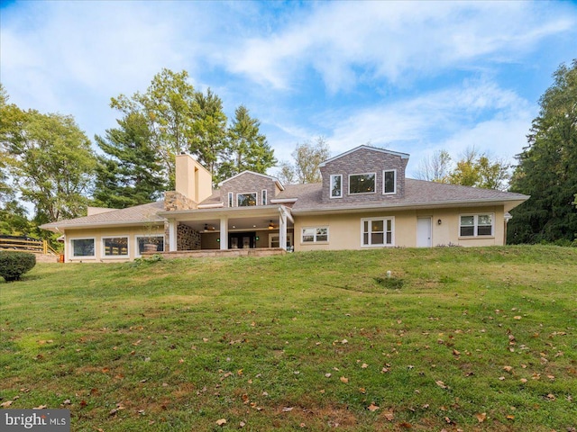 rear view of property featuring a yard, a chimney, and stucco siding