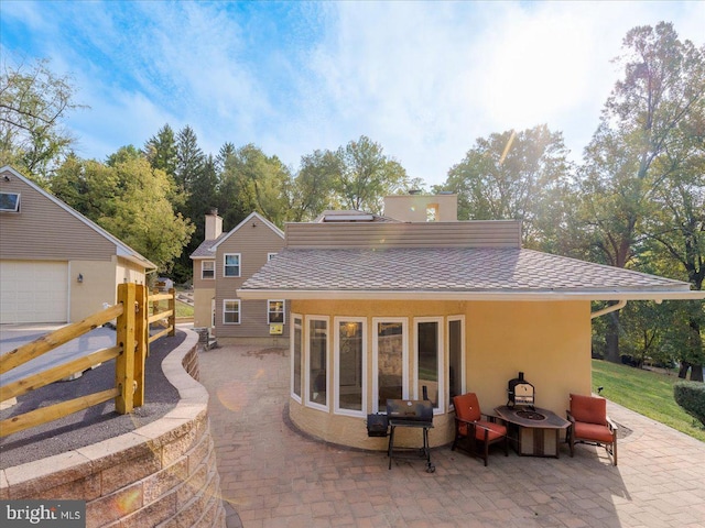 back of property with stucco siding, a shingled roof, a fire pit, and a patio