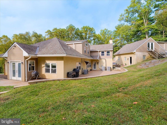 rear view of property featuring a shingled roof, a patio, a lawn, and french doors