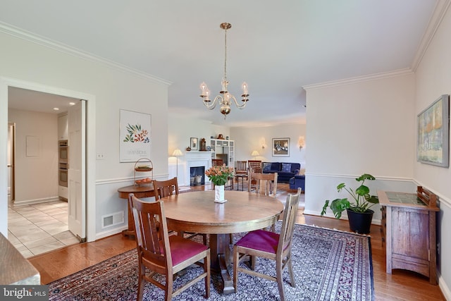 dining area with light wood finished floors, a fireplace, visible vents, and crown molding