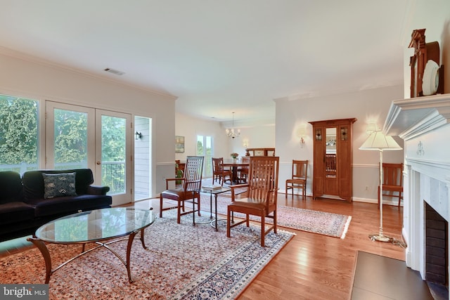 living room with a high end fireplace, a notable chandelier, wood-type flooring, and a healthy amount of sunlight