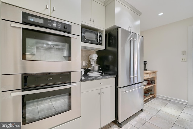 kitchen featuring dark countertops, decorative backsplash, appliances with stainless steel finishes, white cabinetry, and light tile patterned flooring