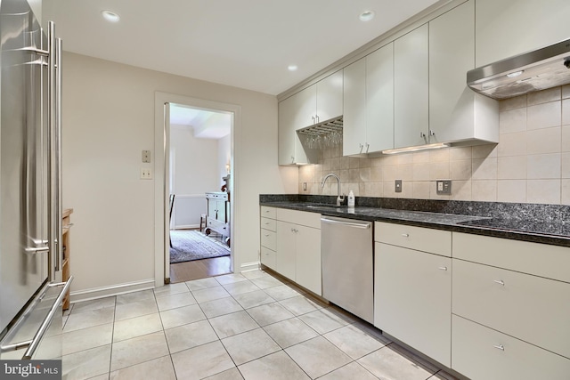 kitchen with decorative backsplash, appliances with stainless steel finishes, light tile patterned flooring, a sink, and exhaust hood