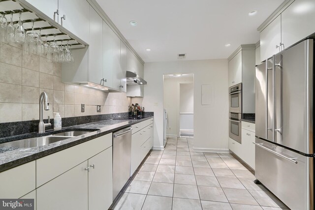 kitchen featuring light tile patterned floors, appliances with stainless steel finishes, sink, dark stone counters, and decorative backsplash