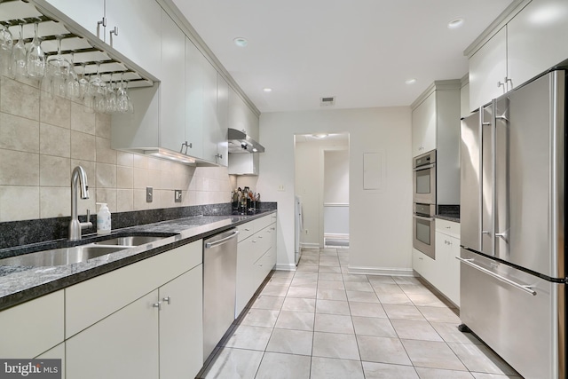 kitchen featuring light tile patterned floors, stainless steel appliances, decorative backsplash, a sink, and dark stone counters