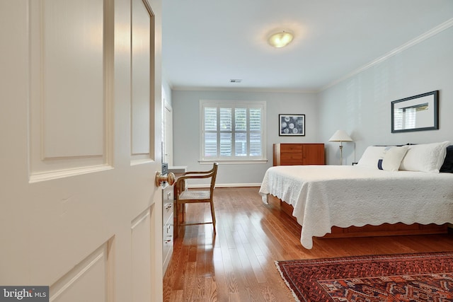 bedroom with ornamental molding, baseboards, visible vents, and hardwood / wood-style floors