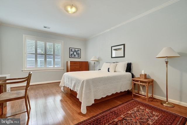 bedroom with ornamental molding, visible vents, baseboards, and wood finished floors