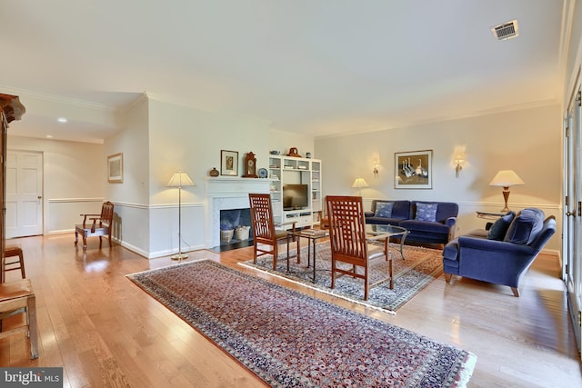 living room with a fireplace with flush hearth, visible vents, baseboards, hardwood / wood-style floors, and crown molding