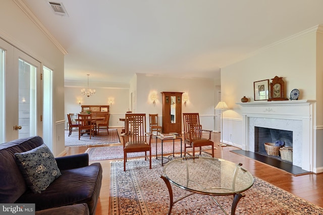 living room featuring crown molding, a notable chandelier, light wood-type flooring, and a high end fireplace