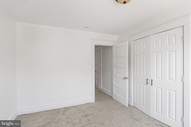 unfurnished bedroom featuring light colored carpet, ornamental molding, and a closet