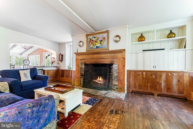 living room with built in features, a warm lit fireplace, lofted ceiling with beams, and hardwood / wood-style flooring