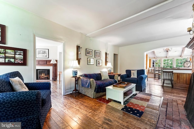 living area featuring a warm lit fireplace, arched walkways, beam ceiling, and hardwood / wood-style flooring