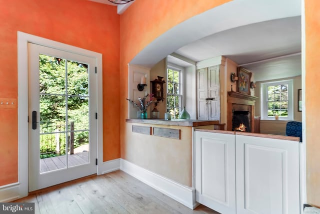 kitchen featuring a warm lit fireplace, white cabinetry, wood-type flooring, baseboards, and arched walkways