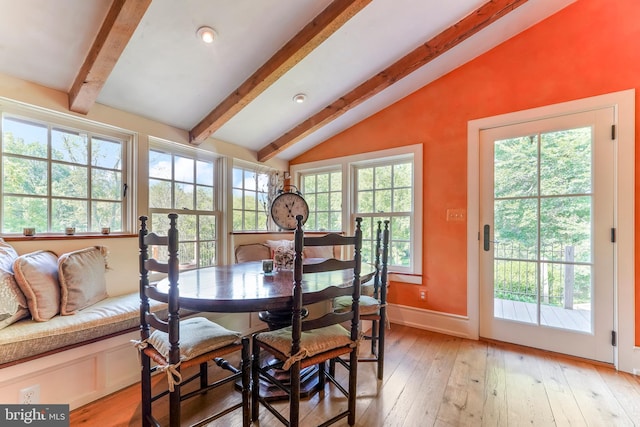 dining room featuring baseboards, vaulted ceiling with beams, a healthy amount of sunlight, and light wood-type flooring