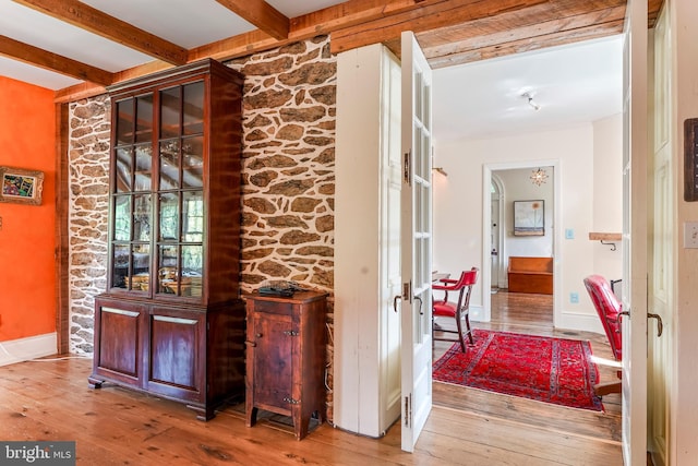 hallway featuring baseboards, light wood-type flooring, and beam ceiling