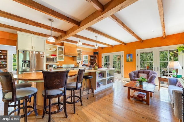 kitchen featuring light wood-type flooring, beamed ceiling, hanging light fixtures, appliances with stainless steel finishes, and french doors