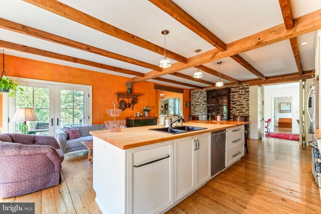 kitchen with pendant lighting, wood counters, white cabinetry, light hardwood / wood-style flooring, and a center island with sink