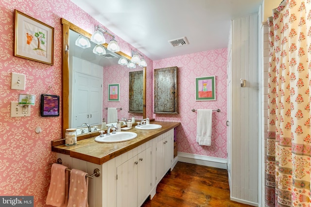 bathroom with a sink, visible vents, wallpapered walls, and wood finished floors