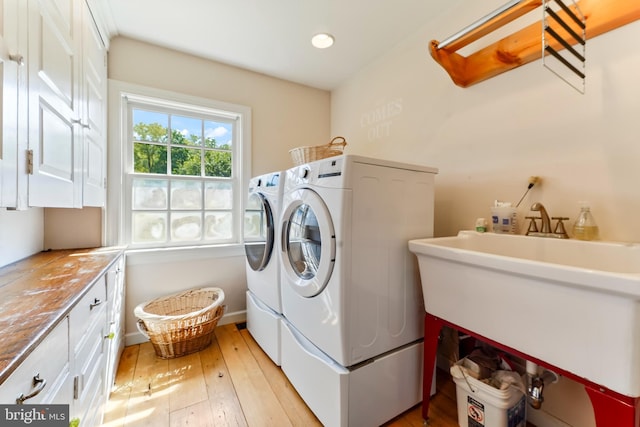 laundry room with baseboards, cabinet space, a sink, light wood-type flooring, and washing machine and dryer