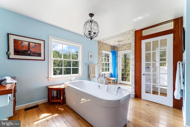 full bath featuring visible vents, a soaking tub, baseboards, a notable chandelier, and wood-type flooring