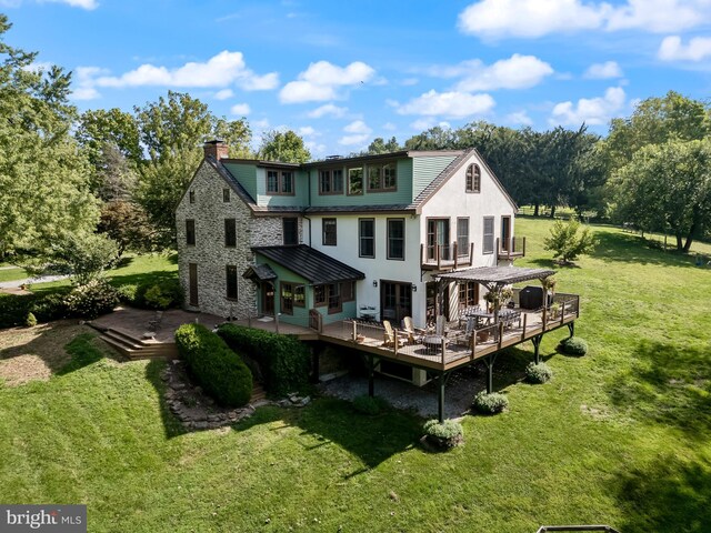 rear view of property featuring stucco siding, a wooden deck, stone siding, a yard, and a chimney