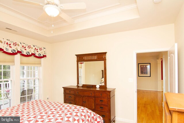 bedroom featuring crown molding, light wood-type flooring, a raised ceiling, and ceiling fan