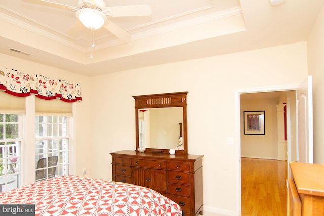 bedroom featuring light wood finished floors, visible vents, baseboards, a tray ceiling, and crown molding