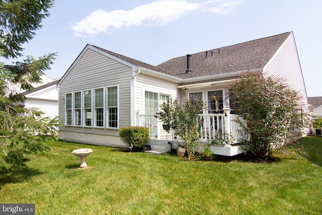 back of house featuring roof with shingles and a lawn