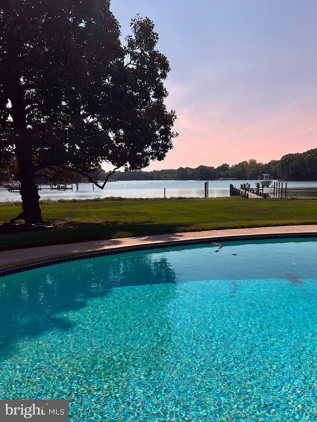 pool at dusk featuring a yard and a water view