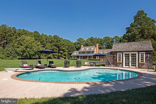 view of swimming pool featuring a yard, a diving board, an outbuilding, and a patio