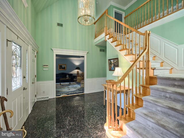 tiled entryway with ornamental molding, a chandelier, and a towering ceiling