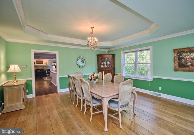 dining area featuring hardwood / wood-style floors, a tray ceiling, an inviting chandelier, and ornamental molding