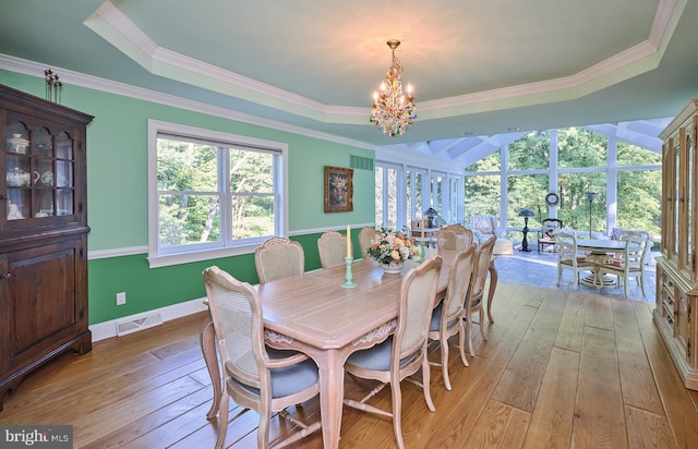 dining space with crown molding, a raised ceiling, an inviting chandelier, and light wood-type flooring