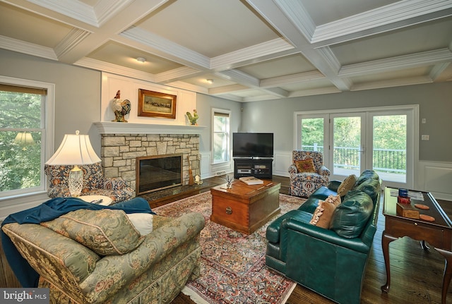 living room featuring beamed ceiling, coffered ceiling, crown molding, wood-type flooring, and a stone fireplace