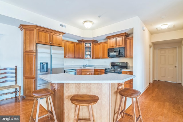 kitchen featuring black appliances, a kitchen bar, a center island, and light hardwood / wood-style floors