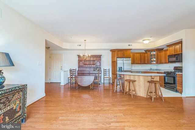 kitchen featuring a breakfast bar area, an inviting chandelier, decorative light fixtures, black appliances, and light hardwood / wood-style floors