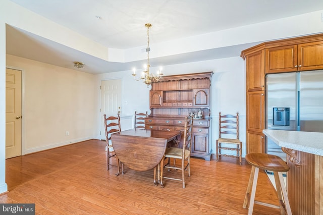 dining space with a raised ceiling, an inviting chandelier, and light hardwood / wood-style floors