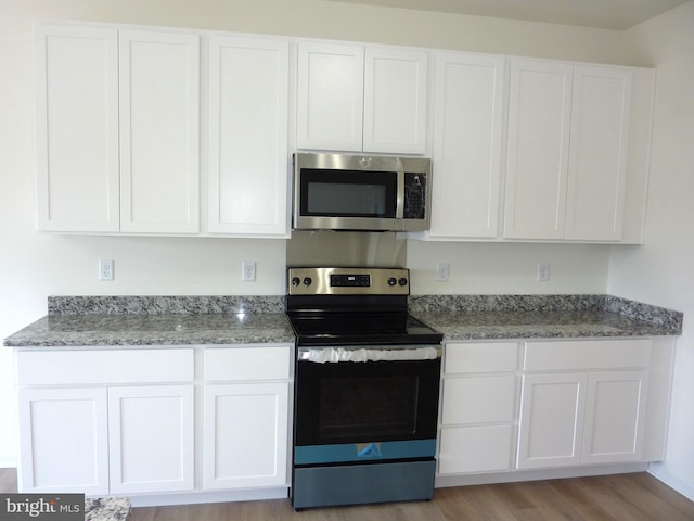 kitchen with appliances with stainless steel finishes, white cabinetry, light wood-style flooring, and light stone counters