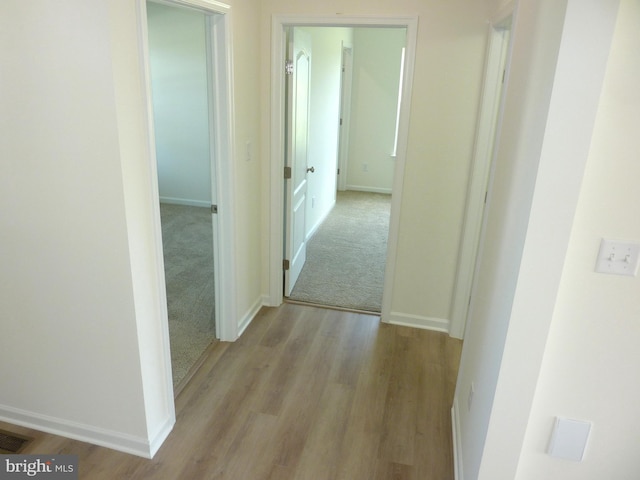 hall with visible vents, baseboards, and wood finished floors