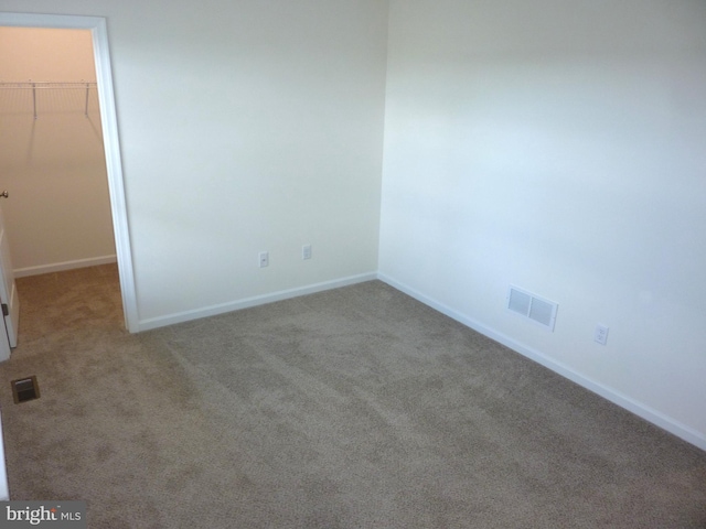 unfurnished bedroom with a walk in closet, visible vents, and carpet flooring