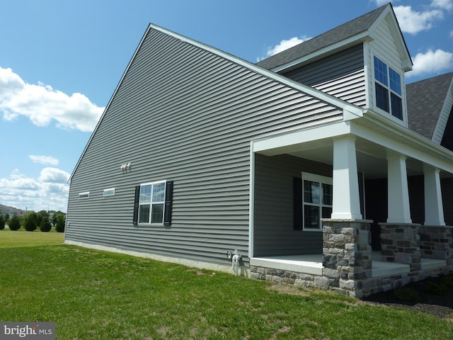 view of side of property featuring covered porch, a shingled roof, and a lawn