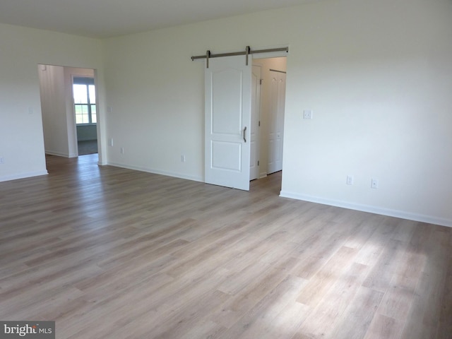 unfurnished room with wood finished floors, baseboards, and a barn door