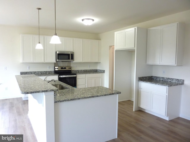 kitchen with appliances with stainless steel finishes, dark stone countertops, wood finished floors, white cabinetry, and a sink