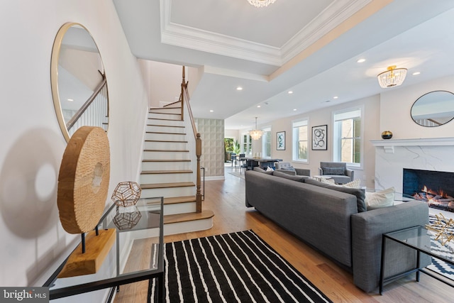 living room featuring light wood-type flooring, a fireplace, crown molding, and a notable chandelier